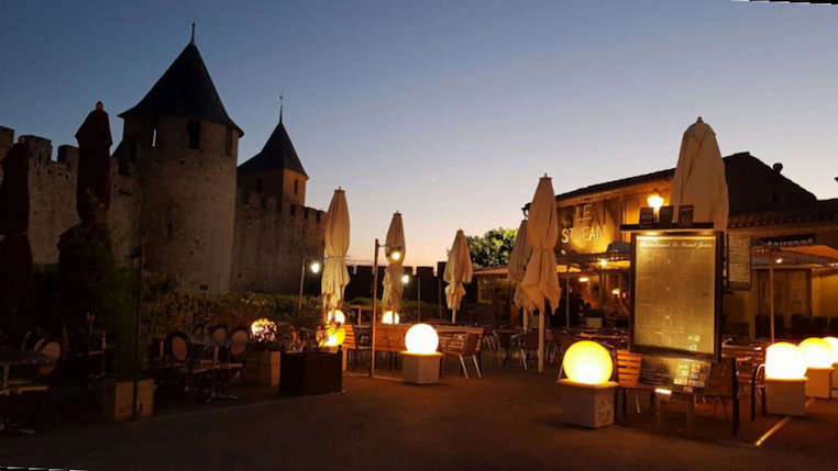 Entrée du restaurant le Sain-Jean éclairée de nuit avec les remparts de la cité de Carcassonne en fond.