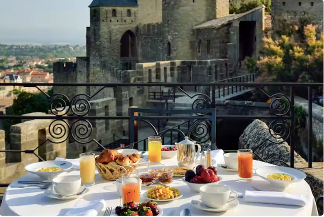 Table avec des assortiments de jus et venoiseries. La table est en hauteur et donne une vue sur la cité de carcasonne et le paysage aux alentour.