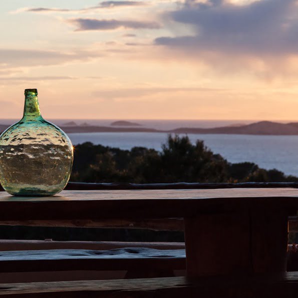 photo sur la terrasse avec un vase qui est déposé sur la grande table en bois la vue est sur le coucher de soleil sur la mer