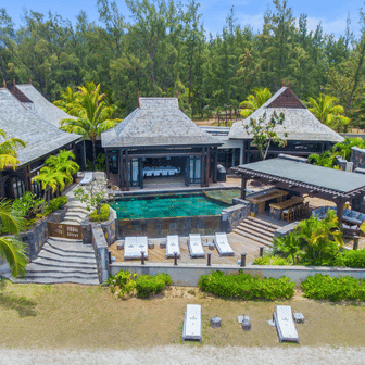 Vue de haut d'une villas en bord de mer avec piscine et transat au bord de la plage