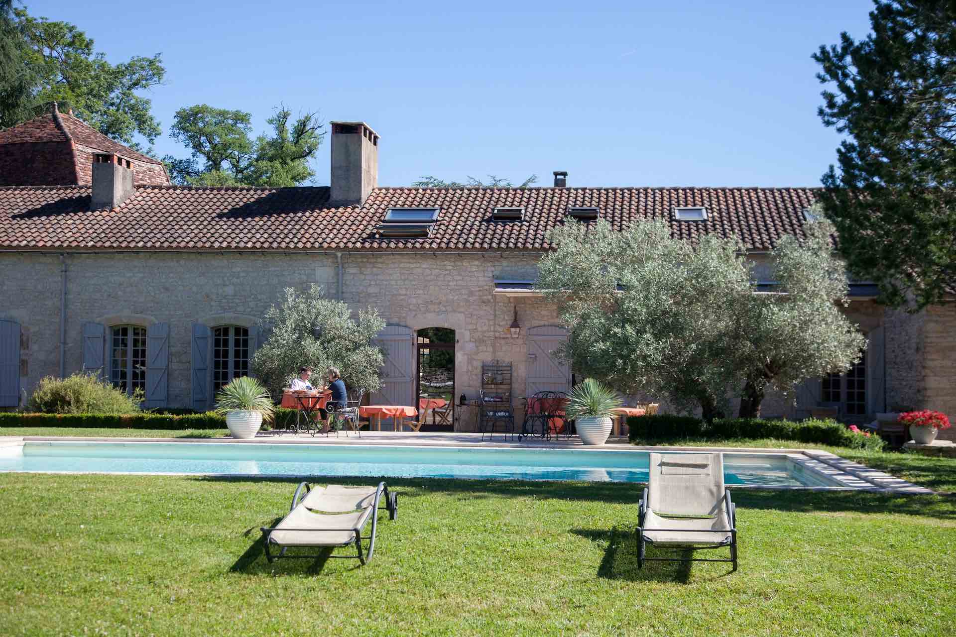 photo prise de loin de la maison principale avec une table, des transats et deux personnes autour d'une table - domaine de labarthe