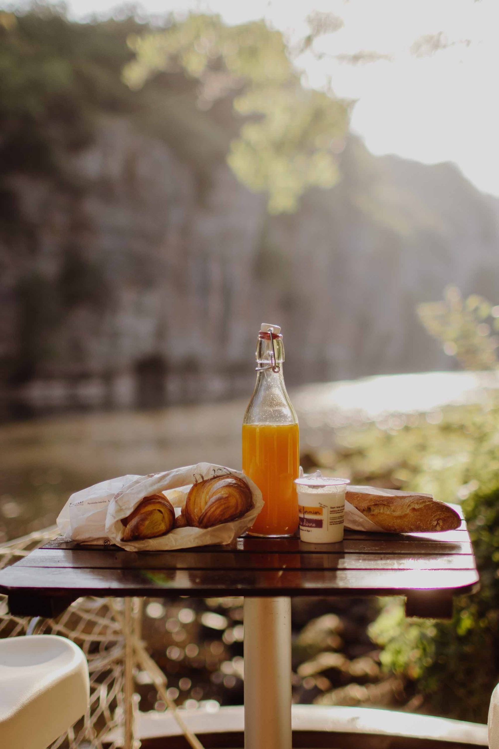 Vue du petit-déjeuner sur le ponton avec le lever du soleil, jus d'orange, croissants, pain et yaourt - Parenthèse Flottante