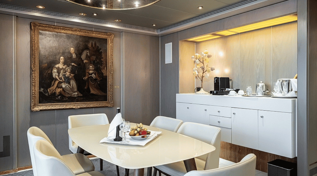 5 chaises autour d'une table avec un assortiment de fruit. Tableau d'une peinture en arrière plan