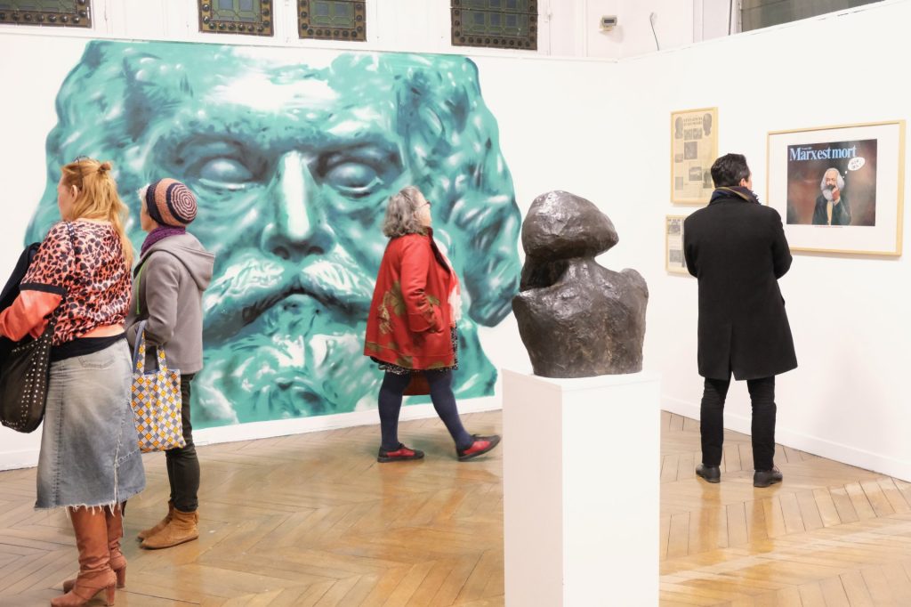personnes regardant une exposition dans une galerie avec tableaux et scultures