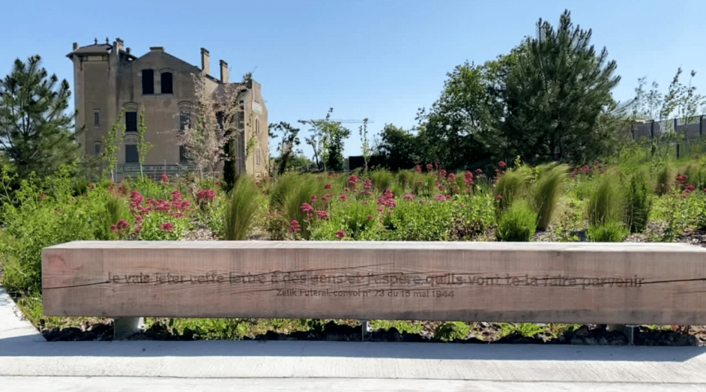 Banc gravé "Je vasi jeter cette lettre à des gens et j'espère qu'ils vont te la faire parvenir" avec en fond l'ancienne gare de déportation de Bobigny