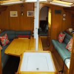 intérieur de la cabine d'un voilier. Table au centre et canapé deux deux côtés avec cuisine équipé à gauche